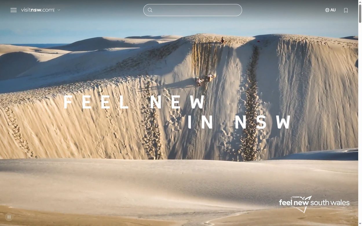 Visit NSW tourism home page with a full screen sand dune video and Feel New in NSW headline